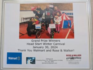 A group of people, including children and adults, pose with a bicycle prize at the Head Start Winter Carnival on January 30, 2024. The sign on the bike acknowledges Walmart and Rose & Walker as sponsors.